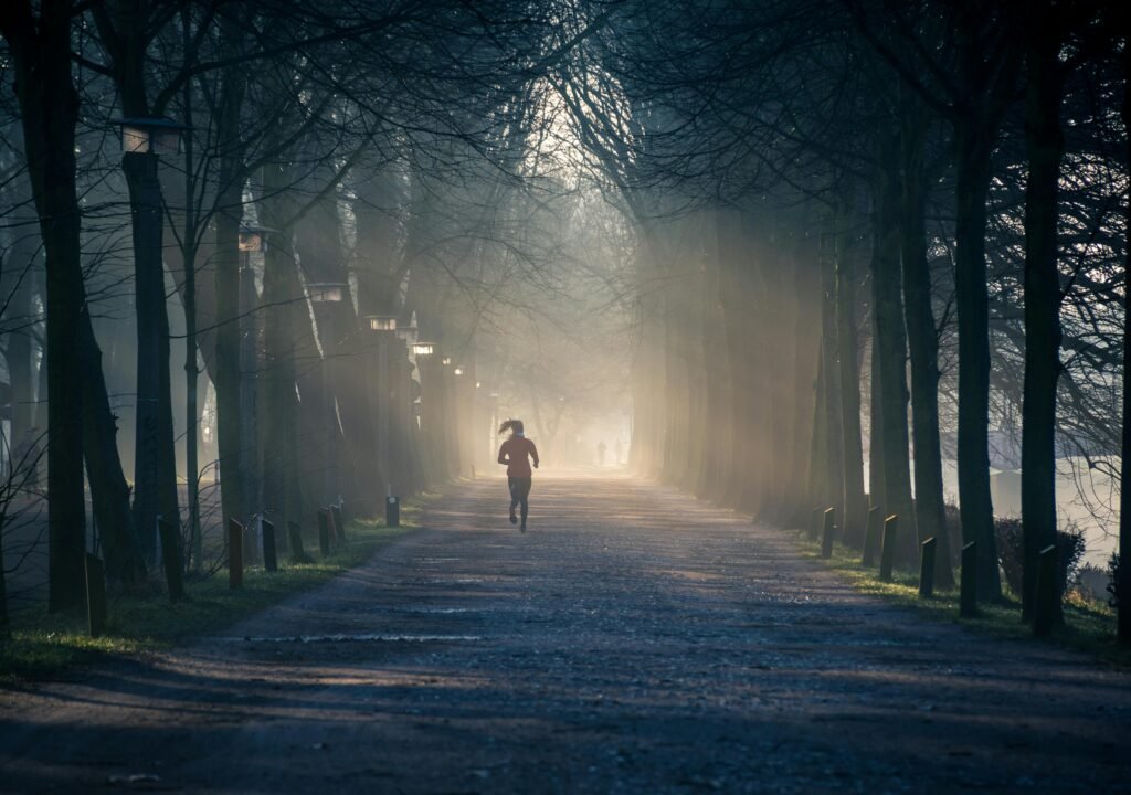 pexels-photo-878151-878151 A person jogging along a foggy tree-lined pathway in a park during sunrise.