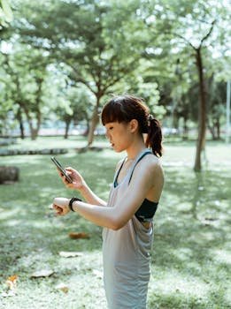 pexels-photo-4436295-4436295 A fit young woman checks her smartwatch while holding a smartphone in a serene park setting.